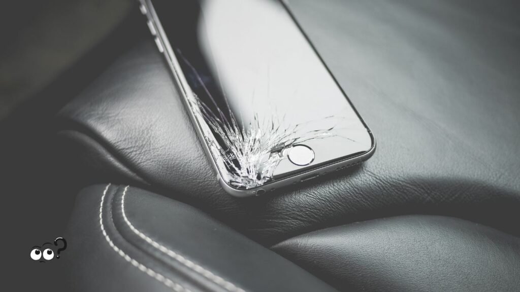 Votre Face ID ne fonctionne plus ? Voici pourquoi et comment le réparer simplement ! 1 un iphone sur la banquette en cuir d'une voiture avec l'écran brisé au niveau du bord inférieur gauche.