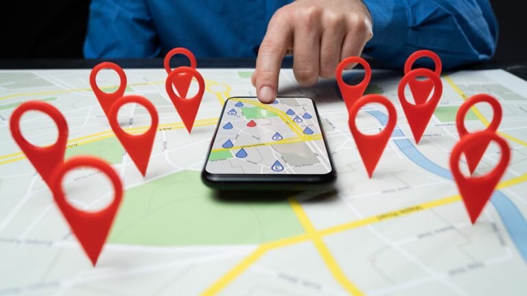 un smartphone avec l'application google maps posé sur une carte papier avec des marqueurs de position sur celle-ci